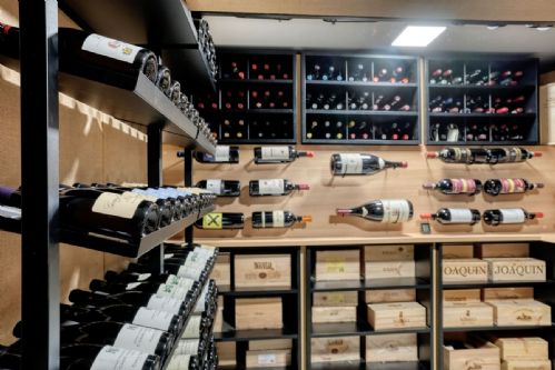 Wine vault a Milano con scaffali in ferro, bottiglie a parete e casse di vino pregiato — Winest