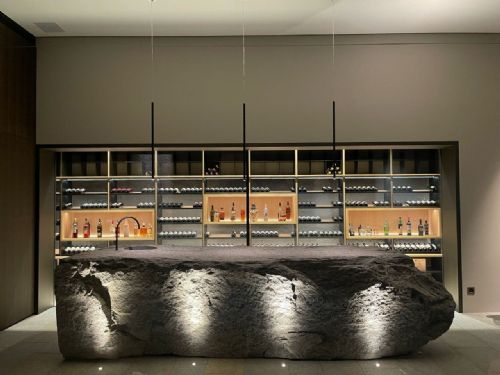 Wine room di design con isola in pietra naturale e parete espositiva illuminata, Svizzera — Winest